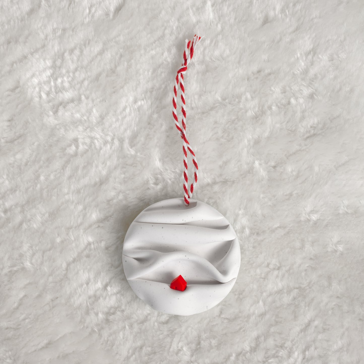 made from polymer clay, its a flat circle ornament with speckles white folds made to look like a snowy landscape, with a red house nestled on a hill, hung with a red and white string