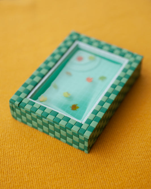 miniature pool with green tiles and fall leaves suspended in the resin water
