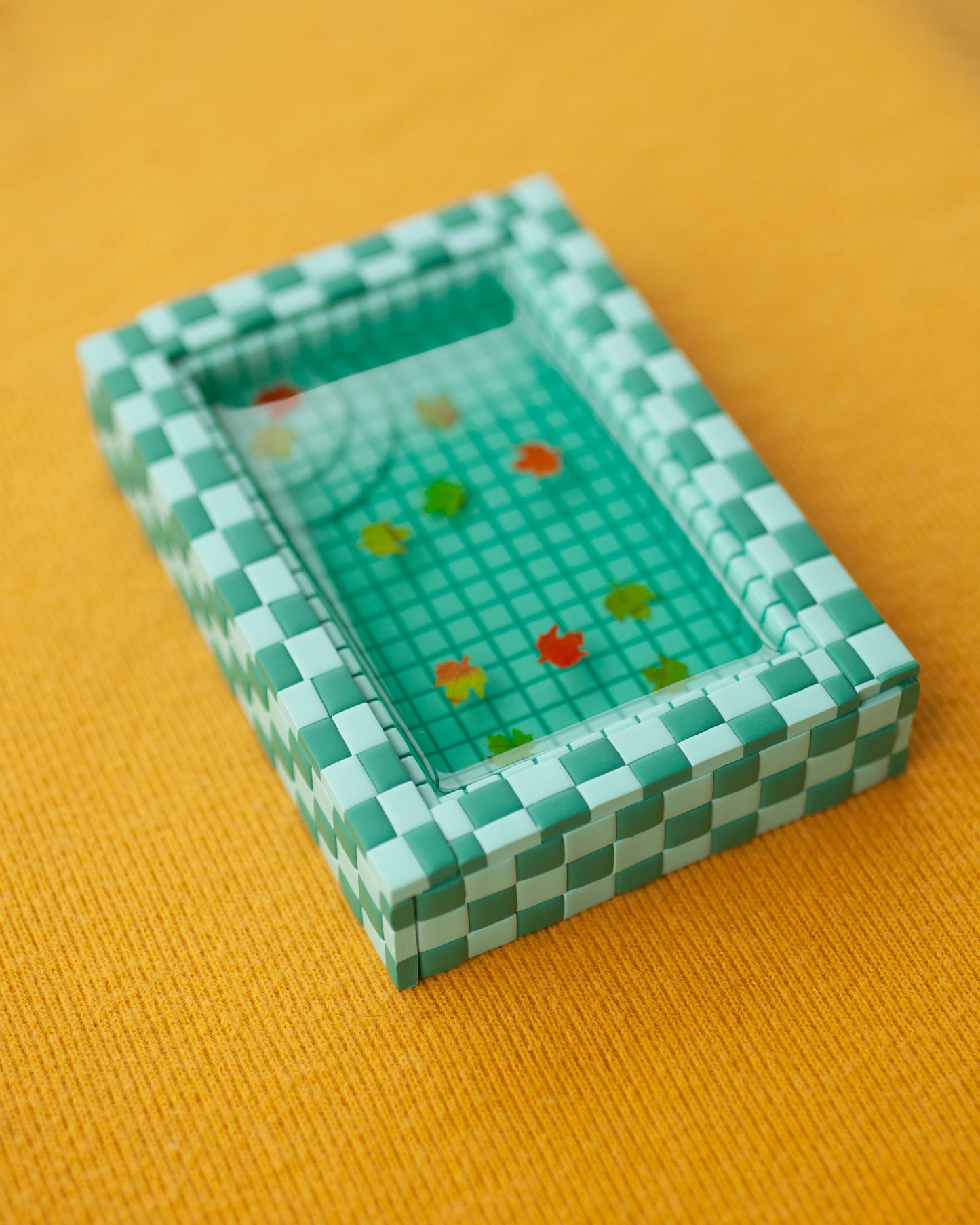 miniature pool with green tiles and fall leaves suspended in the resin water