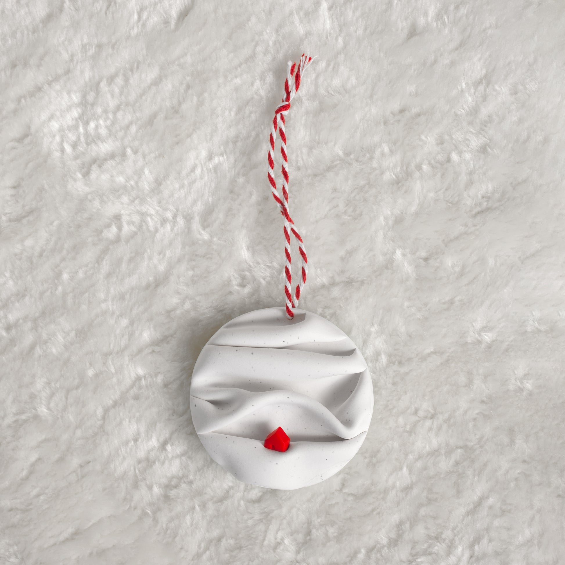made from polymer clay, its a flat circle ornament with speckles white folds made to look like a snowy landscape, with a red house nestled on a hill, hung with a red and white string
