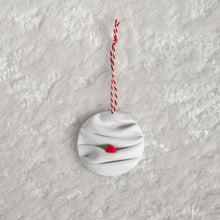 Load image into Gallery viewer, made from polymer clay, its a flat circle ornament with speckles white folds made to look like a snowy landscape, with a red house nestled on a hill, hung with a red and white string
