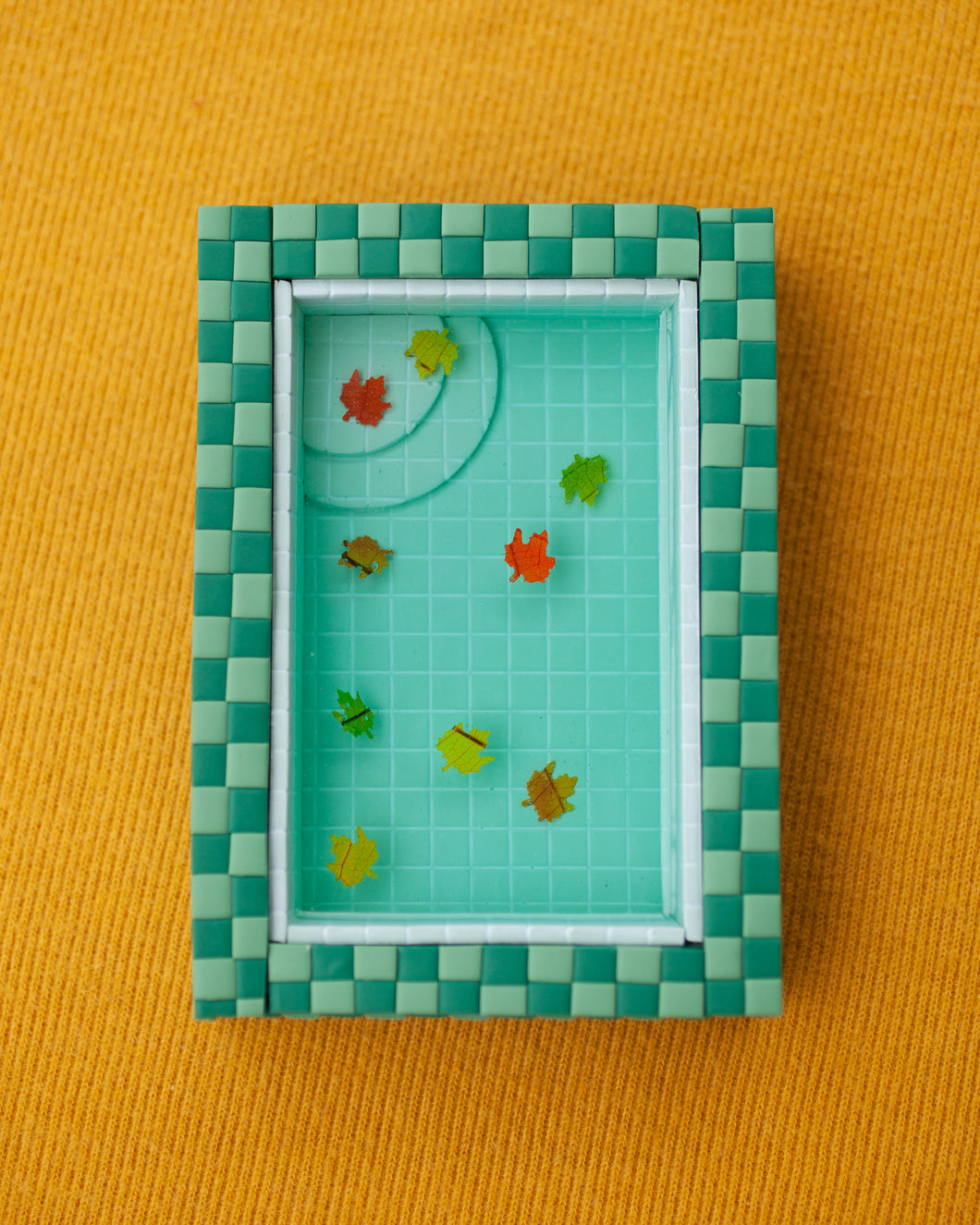 miniature pool with green tiles and fall leaves suspended in the resin water