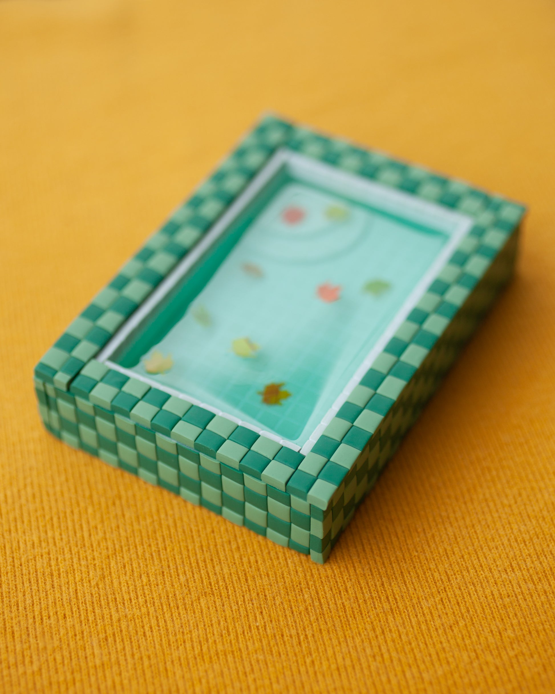 miniature pool with green tiles and fall leaves suspended in the resin water