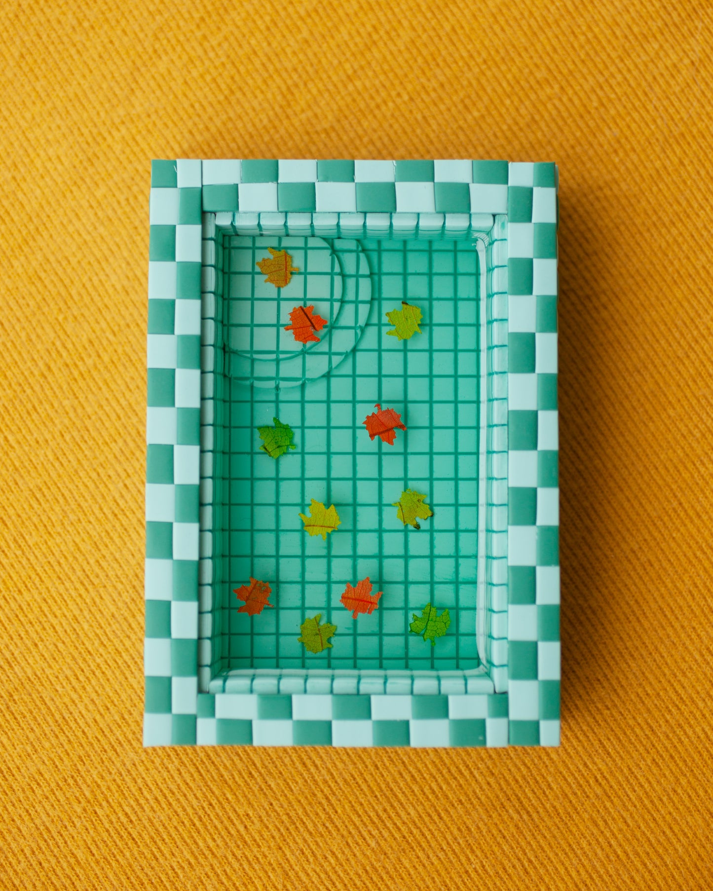 miniature pool with green tiles and fall leaves suspended in the resin water
