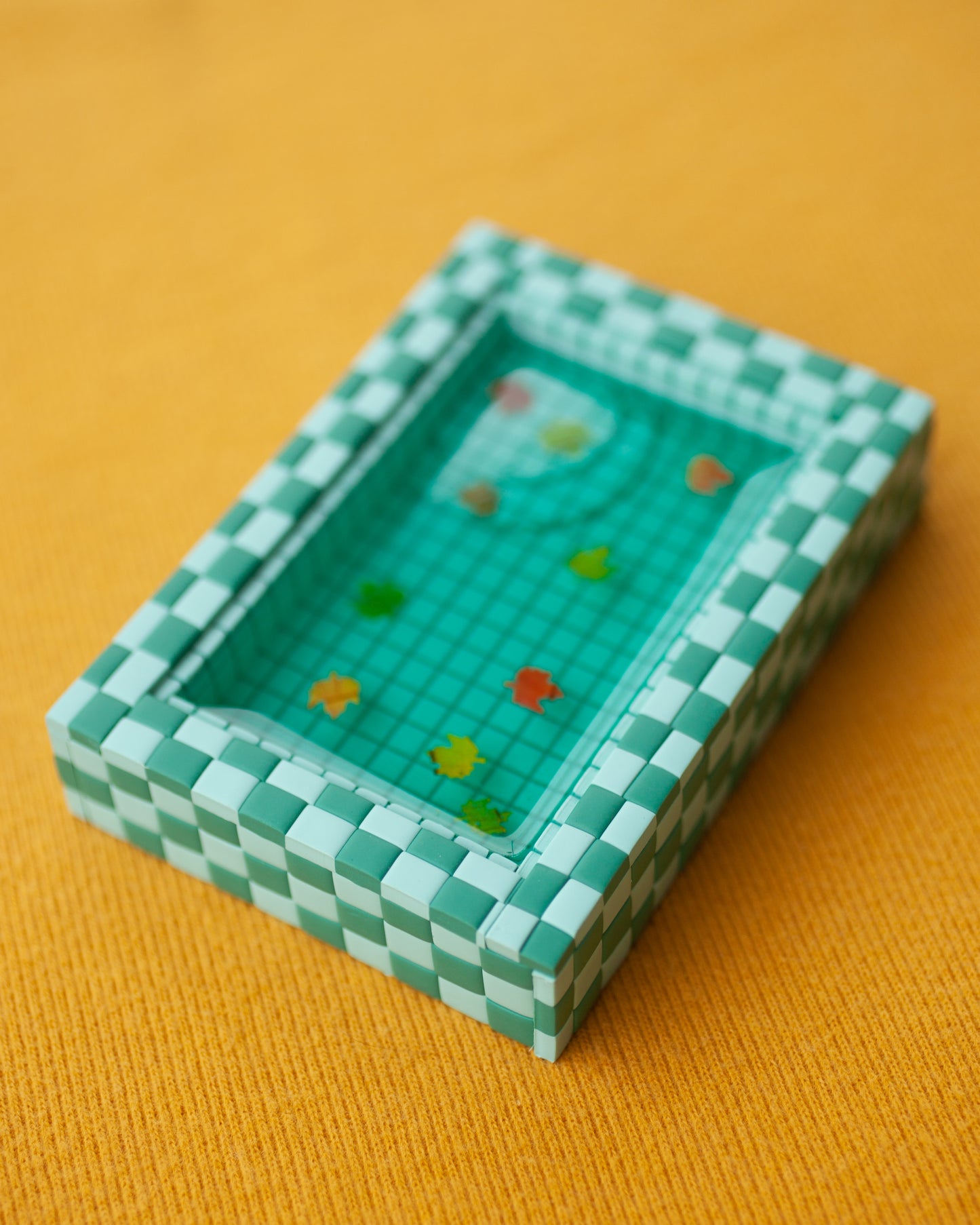 miniature pool with green tiles and fall leaves suspended in the resin water