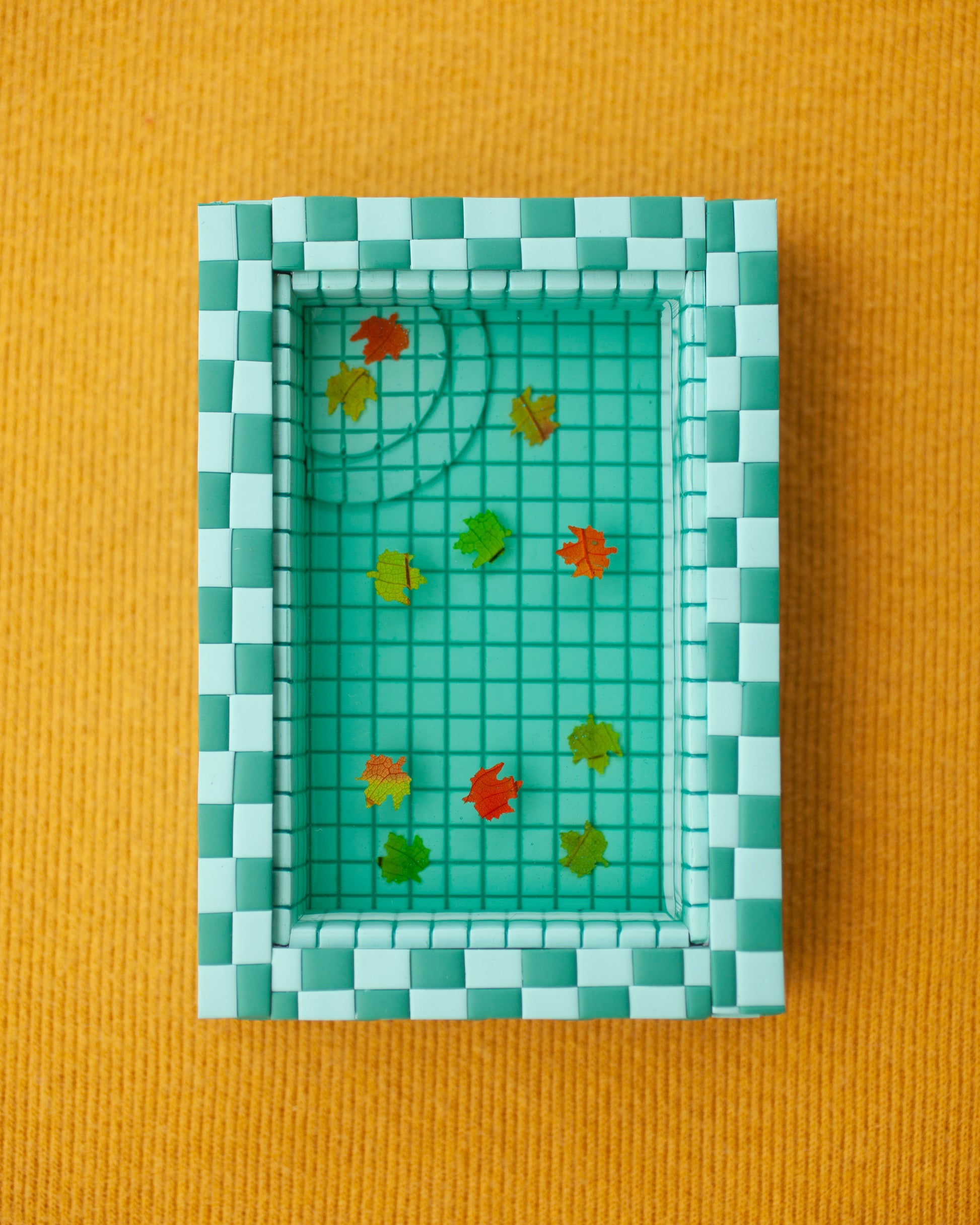 miniature pool with green tiles and fall leaves suspended in the resin water